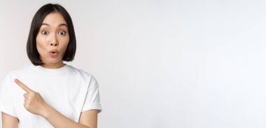 Genç Japon kadının gülümseyişini yakın plan, fotokopi alanına parmak işareti, duyuru ya da reklam afişi, beyaz arka planda duran