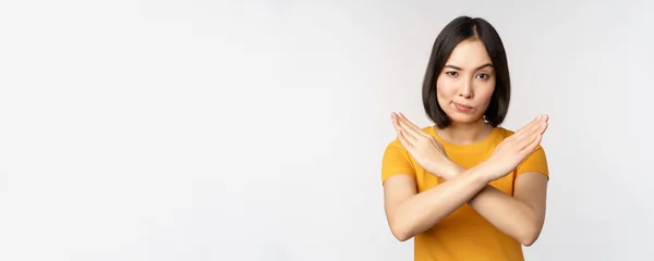 Retrato de mujer asiática mirando seria y enojada, mostrando stop prohibir gesto, signo tabú, prohibiendo smth, de pie en camiseta amarilla sobre fondo blanco —  Fotos de Stock