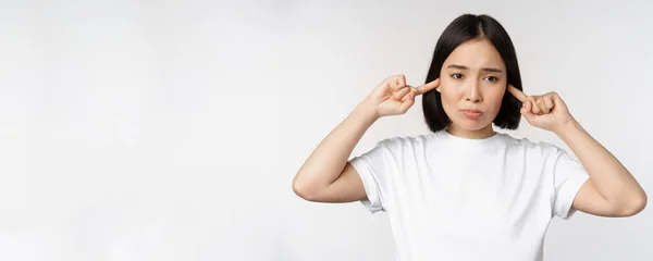 Ritratto di donna asiatica chiuso le orecchie e sensazione di disagio da rumore forte, suono fastidioso, in piedi su sfondo bianco — Foto Stock