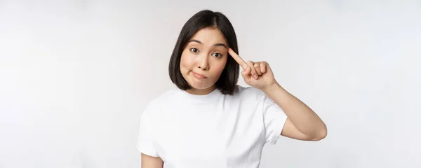 Ma sei impazzito? Giovane donna asiatica rotolare dito sulla testa, prendendo in giro qualcuno stupido, in piedi in t-shirt su sfondo bianco — Foto Stock