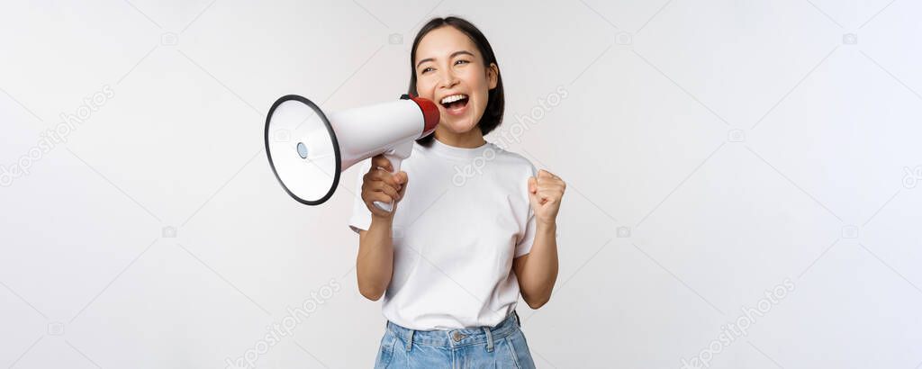 Asian girl shouting at megaphone, young activist protesting, using loud speakerphone, making announcement, white background