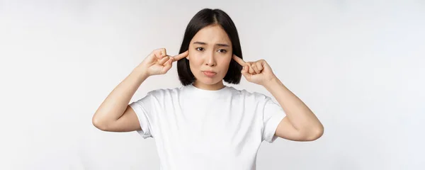 Portrait de femme asiatique fermant les oreilles et sentant l'inconfort du bruit fort, son ennuyeux, debout sur fond blanc — Photo