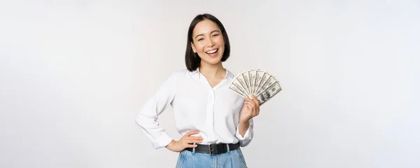 Kredit- och lånebegreppet. Leende ung asiatisk kvinna som innehar kontanter dollar och ser glad ut på kameran, vit bakgrund — Stockfoto