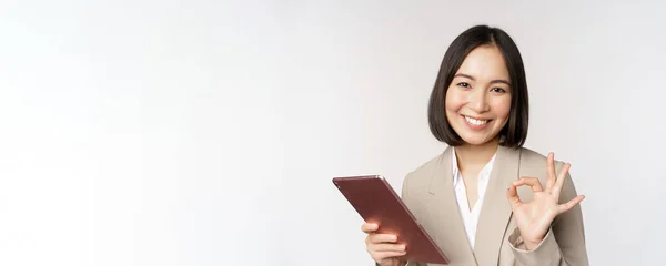 Bild einer erfolgreichen asiatischen Geschäftsfrau, die ein digitales Tablet in der Hand hält, Okay, ok Zeichen zeigt, den Kunden versichert, vor weißem Hintergrund steht — Stockfoto