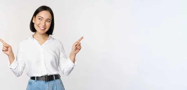 Bild der schönen asiatischen Frau zeigt mit dem Finger nach links und rechts, trifft Entscheidungen, zeigt zwei Varianten Entscheidungen, steht über weißem Hintergrund — Stockfoto