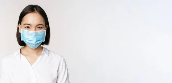 Covid en gezondheidszorg concept. Close-up portret van Aziatische vrouw, kantoor dame in het gezicht masker, glimlachen, met behulp van bescherming tegen coronavirus tijdens pandemie, witte achtergrond — Stockfoto