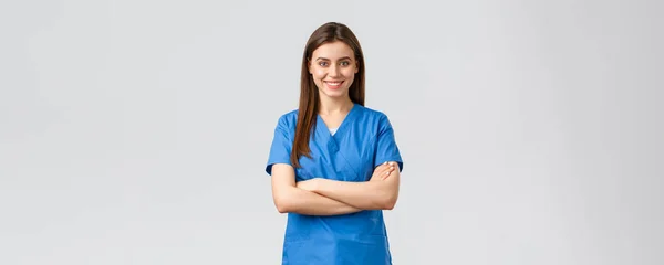 Медицинские работники, предотвратить вирус, страхование и медицина концепции. Уверенная в себе женщина-врач, медсестра в синем халате, улыбающаяся и скрещивающая руки грудь, готовая спасать жизни пациентов, серый фон — стоковое фото