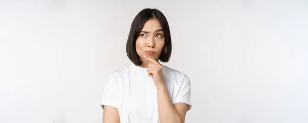 Femme asiatique réfléchie regardant de côté, réfléchissant, faisant des suppositions, pensant ou choisissant smth, debout sur fond blanc — Photo