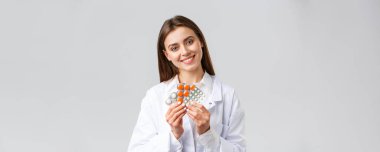 Eczane, sağlık çalışanları, sigorta ve hastane konsepti. Beyaz önlüklü yakışıklı doktor, gülümseyen kadın doktor ya da eczacı, ilaç gösteriyor, farklı haplar ya da antibiyotikler.