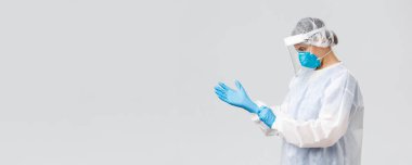 Covid-19, virüsün önlenmesi, sağlık, sağlık çalışanları ve karantina konsepti. Kişisel koruyucu ekipman içinde genç bir doktor, hemşire Coronavirus hastasıyla çalışmak için lastik eldiven taktı.