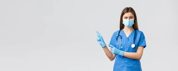 Covid-19，防止病毒、健康、保健工作者和检疫概念。忧心忡忡的蓝衣女护士，戴着医疗面具的医生，皱着眉头，指着糟糕的信息 — 图库照片