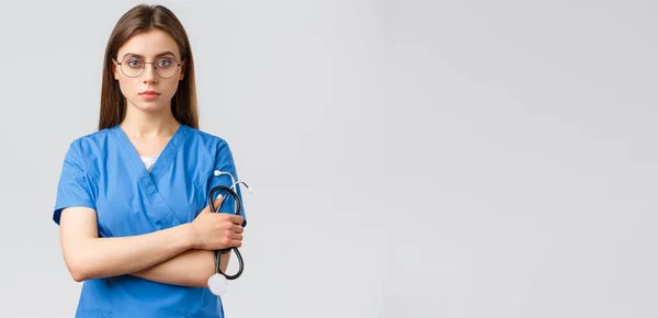 Egészségügyi dolgozók, orvostudomány, biztosítás és a kovid-19 világjárvány koncepciója. Komoly és határozott, hivatásos női ápolónő, orvos kék köpenyben, kezében sztetoszkóppal, szemüveget visel, magabiztosnak látszik — Stock Fotó