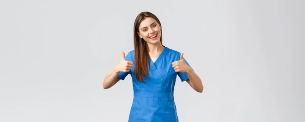 Trabajadores de la salud, prevenir virus, seguros y concepto de medicina. Enfermera optimista y entusiasta, doctora en uniformes azules, pulgares arriba y sonriente, anima a los pacientes a quedarse en casa —  Fotos de Stock