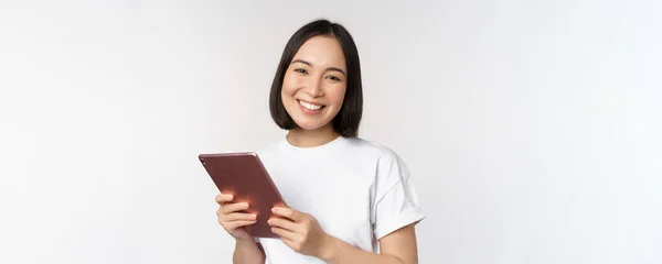 디지털 태블릿을 가지고 행복해 보이고 웃으며 웃고 있는, 하얀 배경 위에 티셔츠를 입고 있는, 아시아 소녀의 웃는 모습 — 스톡 사진