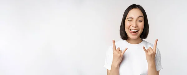 Sassy asian girl shouting, enjoying concert or festival, showing rock on, heavy metal sign, having fun, standing over white background — Stock Photo, Image