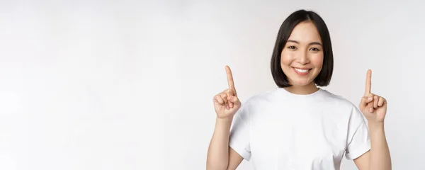 열정적 인 젊은 여성, 손가락을 들고 웃으며 위로 광고를 내보이며 하얀 배경 위에 서 있는 아시아 소녀의 모습 — 스톡 사진