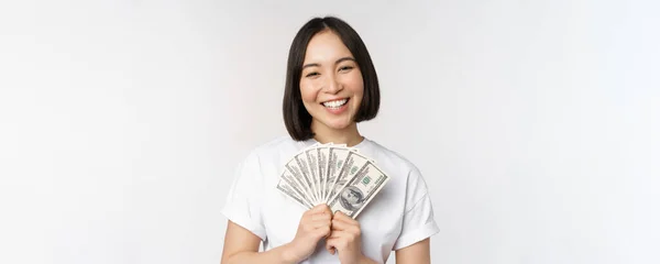 Porträtt av leende asiatisk kvinna som innehar dollar pengar, begreppet mikrokrediter, ekonomi och kontanter, stående över vit bakgrund — Stockfoto