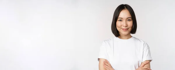 Retrato de cerca de chica coreana confiada, estudiante mirando a la cámara con sonrisa complacida, brazos cruzados en el pecho, de pie sobre fondo blanco — Foto de Stock