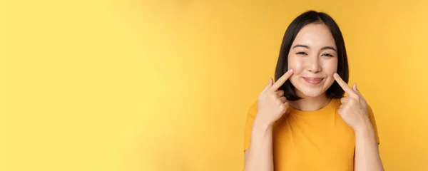 Крупним планом портрет милої азіатської дівчини, що показує її тьмяні і усміхнені кокетливі на камеру, стоїть над жовтим тлом — стокове фото