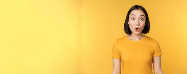 Образ азіатської дівчини виглядає здивованою, реагує здивовано, піднімаючи брови вражені, стоячи над жовтим тлом — стокове фото