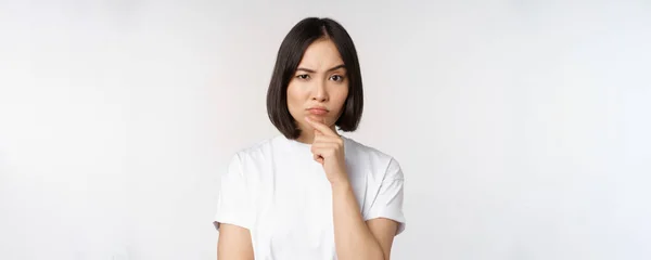 Gedachte aziatische vrouw kijken opzij, nadenken, het maken van veronderstelling, denken of kiezen smth, staande over witte achtergrond — Stockfoto