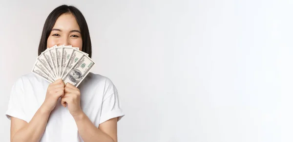 Portrait of smiling asian woman holding dollars money, concept of microcredit, finance and cash, standing over white background — Stock Photo, Image