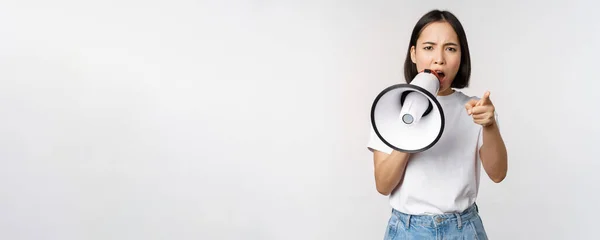 Arg asiatisk kvinna med megafon, skällande, anklagar någon, protesterar med högtalartelefon på protest, står över vit bakgrund — Stockfoto