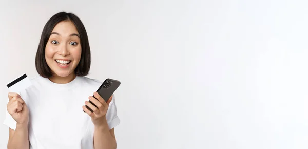 Compras online. Feliz mulher asiática usando cartão de crédito e aplicativo de smartphone, pagando no site via telefone celular, fundo branco — Fotografia de Stock