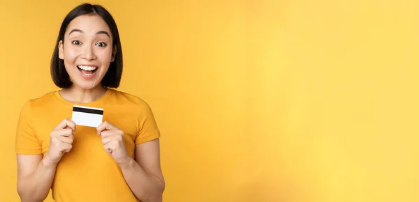 Hermosa mujer asiática mostrando tarjeta de crédito y sonriendo, recomendando servicio bancario, de pie sobre fondo amarillo — Foto de Stock