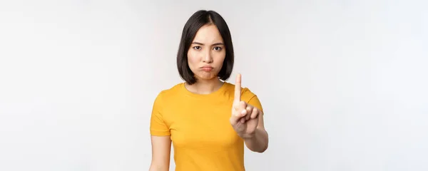 Porträt einer asiatischen Frau, die ernst und wütend guckt, Stoppverbotsgeste zeigt, Tabuzeichen, Verbotsschilder, im gelben T-Shirt vor weißem Hintergrund stehend — Stockfoto