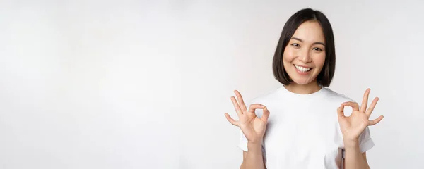 Muy bien, excelente. sonriente asiático mujer mostrando ok signo, aprobación, ok gesto, buscando satisfecho, recomendando smth, de pie sobre blanco fondo — Foto de Stock