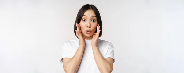 Close-up portret van aziatische meisje kijken verrast, wow gezicht, reageren verbaasd op smth, staan in wit tshirt over studio achtergrond, geïsoleerd — Stockfoto