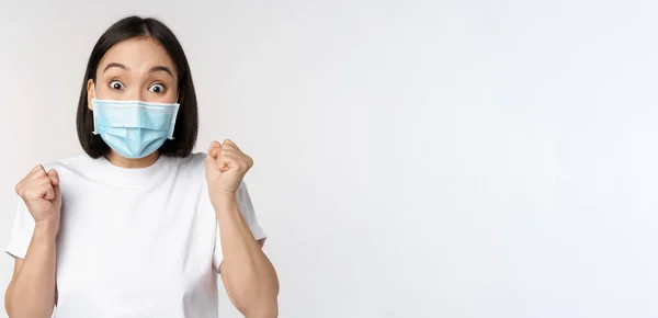 Covid-19, conceito médico e de saúde. Entusiasta mulher asiática em máscara facial médica, dançando e celebrando, ganhando, alcançar objetivo, de pé sobre fundo branco — Fotografia de Stock