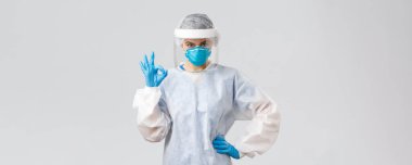 Covid-19, virüsün önlenmesi, sağlık, sağlık çalışanları ve karantina konsepti. Ciddi doktor, PPE 'deki profesyonel hemşire, koruyucu giysi, solunum cihazı ve eldivenler, tamam işareti yap, garanti