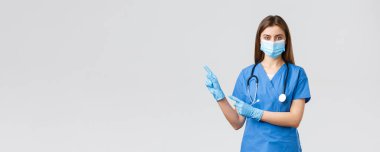 Covid-19, virüsün önlenmesi, sağlık, sağlık çalışanları ve karantina konsepti. Mavi önlüklü, tıbbi maskeli ve eldivenli hoş bayan doktor veya hemşire, takip sayfasına veya linke tıklayarak solu işaret edin.
