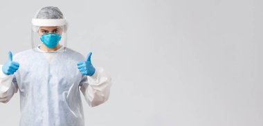 Covid-19, virüsün önlenmesi, sağlık, sağlık çalışanları ve karantina konsepti. Kararlı, kendine güvenen doktor, koruyucu ekipman hemşiresi, solunum cihazı ve eldivenler, baş parmağınızı kaldırın, Corona 'yla savaşın.