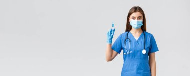 Covid-19, virüsün önlenmesi, sağlık, sağlık çalışanları ve karantina konsepti. Mavi önlüklü ciddi bir kadın hemşire. Doktor maske takıyor. Elinde Coronavirus aşısı şırıngası tutuyor.