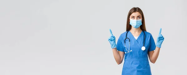 Covid-19，防止病毒、健康、保健工作者和检疫概念。好奇的女医生或护士，身穿蓝色的刷子，戴着医学面罩，高举横幅，手指向上 — 图库照片