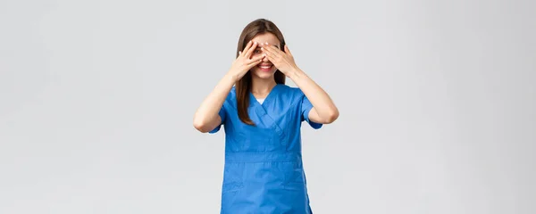 Pracownicy służby zdrowia, zapobiegać wirusom, ubezpieczenia i koncepcji medycyny. Słodka pielęgniarka lub lekarz w klinice, nosząca fartuchy, zakrywająca oczy i zaglądająca przez palce z zaintrygowanym uśmiechem — Zdjęcie stockowe