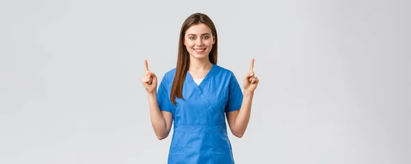 Sağlık çalışanları, virüsü, sigortayı ve ilaç konseptini engelleyin. Mavi önlüklü çekici hemşire ya da doktor, parmaklarını kaldırıp gülümsüyor, reklam pankartı, tıbbi haplar, gri arka plan — Stok fotoğraf
