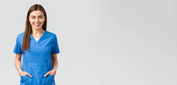 Lucrătorii din domeniul sănătății, previn conceptul de virus, asigurare și medicină. Vesel zâmbind frumos doctor, asistentă medicală de sex feminin în scrubs albastru, stagiar în spital rămânând pozitiv, în picioare fundal gri — Fotografie, imagine de stoc