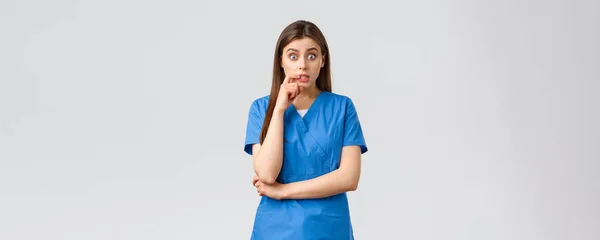 Travailleurs de la santé, prévenir le virus, concept d'assurance et de médecine. Intriguée femme médecin ou infirmière en blouse bleue avoir une conversation avec un collègue, mordre les lèvres, bavarder, lever les sourcils amusé — Photo