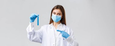 Covid-19, virüsü önleme, sağlık çalışanları ve karantina konsepti. Kişisel koruyucu ekipman doktoru, tıbbi maske ve önlük uzmanı, test tüpü koronavirüs aşısını işaret eden