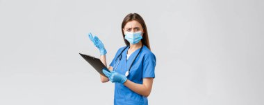 Covid-19, virüsün önlenmesi, sağlık, sağlık çalışanları ve karantina konsepti. Mavi önlüklü ve tıbbi maskeli kadın hemşire ya da doktor, panoda saçma sapan şeyler okuyor.