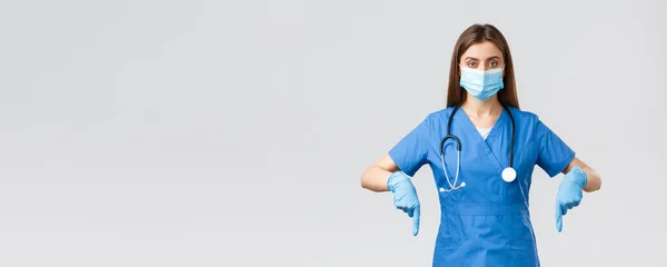 Covid-19，防止病毒、健康、保健工作者和检疫概念。有决心的女护士或医生，身穿蓝色的刷子，戴着医疗面罩和手套，手指朝下，展示信息横幅 — 图库照片