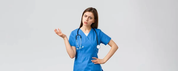 Healthcare workers, prevent virus, insurance and medicine concept. Confused and puzzled female nurse, doctor in scrubs with stethoscope, shrugging and lift hand, stare indecisive, cant understand — Stock Photo, Image