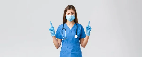 Covid-19 、ウイルス、健康、医療従事者および検疫の概念を防止する。青い頭皮と医療マスクの懐疑的な女性看護師は、この情報を信じていません,疑わしい指を指して — ストック写真