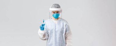 Covid-19, tıbbi araştırma, teşhis, sağlık çalışanları ve karantina konsepti. Ciddi doktor ya da hemşire kişisel koruyucu ekipman, yüz kalkanı elinde Coronavirus aşısı olan bir şırınga