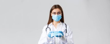 Covid-19, virüsü önleme, klinik, sağlık çalışanları ve karantina konsepti. Tıbbi maskeli, eldivenli, beyaz önlüklü, hastalara yüz maskesi koruması yapan genç doktor, ciddi görün.
