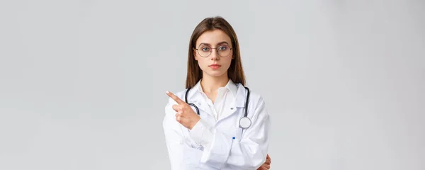 保健工作者、医药、保险和covid-19大流行病概念。相貌严肃的专业女医生，戴着白色刷子和眼镜的护士，手指指向横幅或诊所信息 — 图库照片
